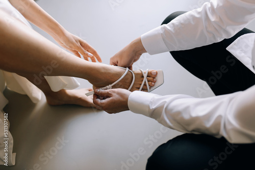 A man helps his future wife to fasten her sandals, a beautiful conceptual wedding photo