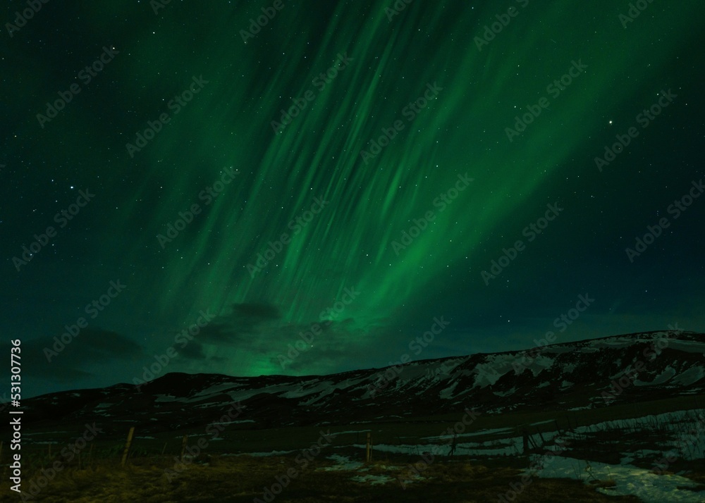 Fototapeta premium Scenic shot of the Aurora Borealis above snowy-covered mountains during nighttime