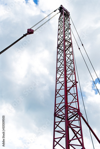 A contrasting shot of a metal crane, red iron structure showing strong angles of the beams and chains. Taken with cumulus cloud and sunlight shining through adding to the dramatic effect. copy space