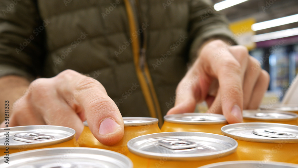 Close-up of many orange cans of beer and a male buyers hands taking a couple