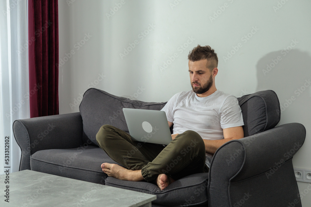 Young smiling man relaxing working with laptop and video conference at home. Young creative man looking at screen message using smartphone.Work from home Young smiling man relaxing working with laptop and video conference at home. Young creative man looking at screen message using smartphone.Work from home