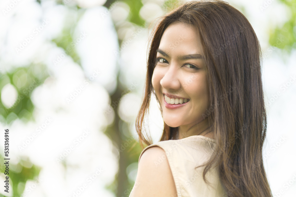 Portrait shot of happy, successful, attractive Asian woman having big smiling and nice teeth with confident look toward the camera at a blurry park background with copy space in natural sunlight. Portrait shot of happy, successful, attractive Asian woman having big smiling and nice teeth with confident look toward the camera at a blurry park background with copy space in natural sunlight.