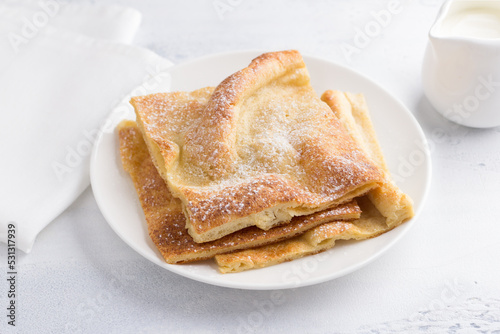A plate of traditional finnish or danish pancakes pannukakku sprinkled with powdered sugar with sour cream and jam on a light background. Delicious vegetarian homemade breakfast