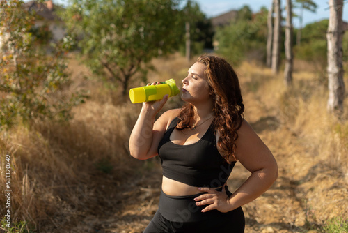 Canvas Print young overweight woman drinking water after jogging in the forest