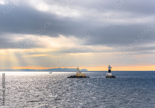 Lighthouse and oceanographic observation station of Ashikashima in the sea of the Uraga channel of Tokyo bay with a boat sailing along the Boso peninsula coasts in the morning light below a cloudy sky photo