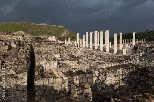 Ruins of ancient Scythopolis with a colonnade brightly illuminated by the sun against a stormy sky, Beth-shean
