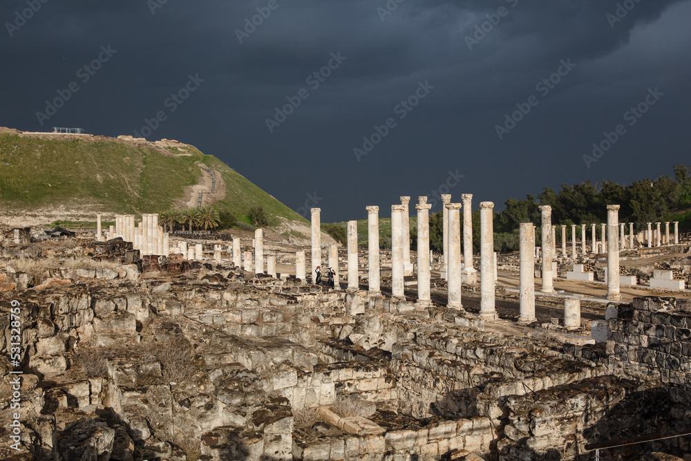 Ruins of ancient Scythopolis with a colonnade brightly illuminated by the sun against a stormy sky, Beth-shean