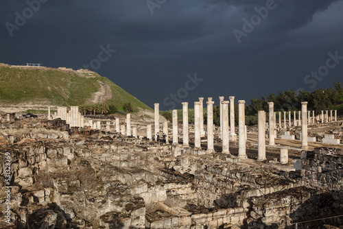 Ruins of ancient Scythopolis with a colonnade brightly illuminated by the sun against a stormy sky, Beth-shean