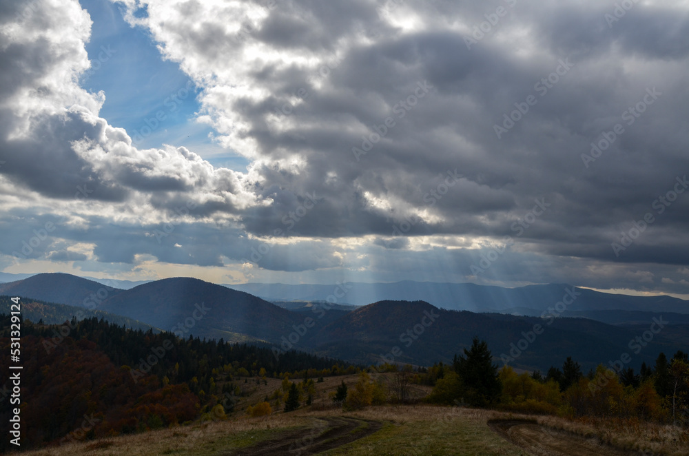 Scenic autumn mountain landscape with rays of light through cloudy sky. Carpathian Mountains, Ukraine