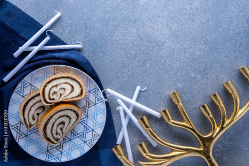 Hanukkah desert plate with nut roll , white candles, and golden menorah on textured blue background photo