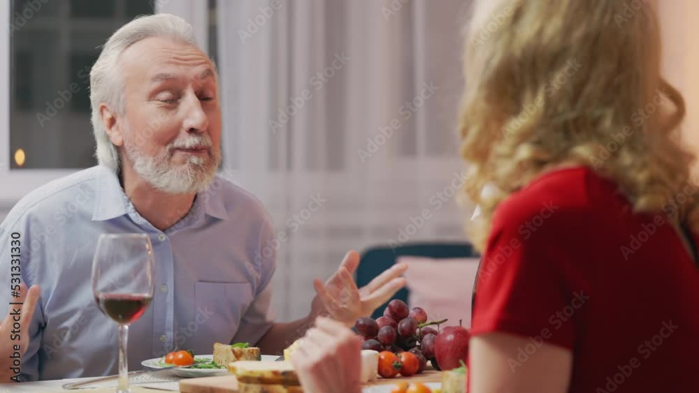 Cheerful senior man telling funny story to wife during romantic supper, date Cheerful senior man telling funny story to wife during romantic supper, date