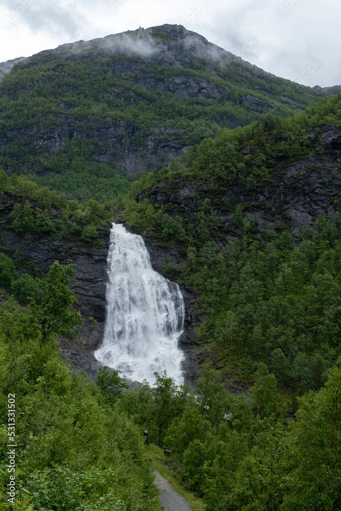 Wonderful landscapes in Norway. Hordaland. Beautiful scenery of Fossen Bratte (Brattefossen) waterfall from the Eikedalselva river. Mountains, trees in background. Rainy day. Selective focus Wonderful landscapes in Norway. Hordaland. Beautiful scenery of Fossen Bratte (Brattefossen) waterfall from the Eikedalselva river. Mountains, trees in background. Rainy day. Selective focus