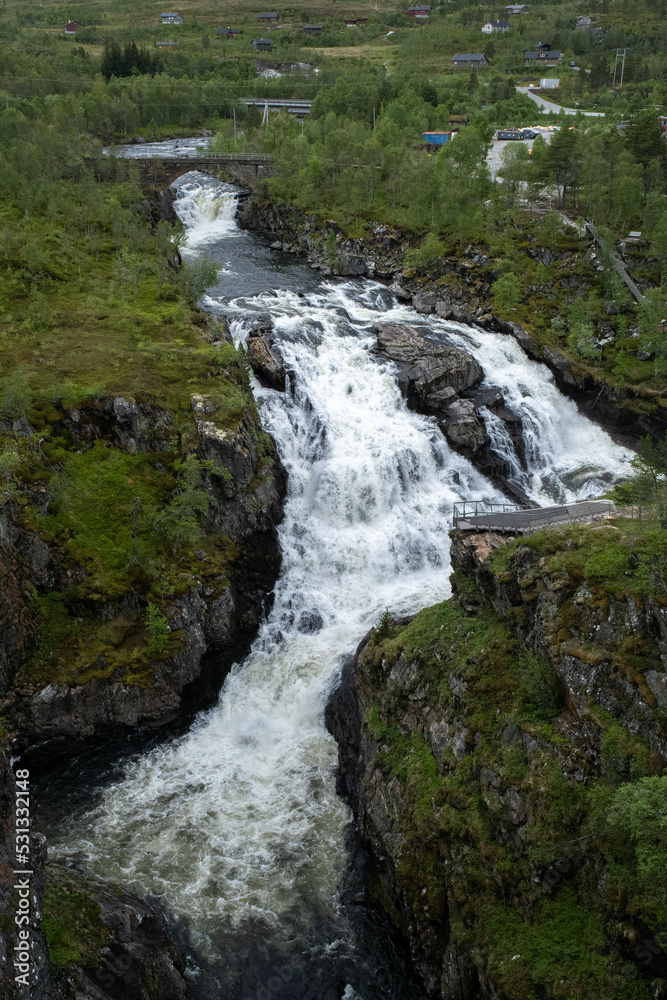 Wonderful landscapes in Norway. Vestland. Beautiful scenery of Voringfossen waterfall in the Mabodalen valley on the Hardanger scenic route. Mountains, trees in background. Cloudy day. Selective focus