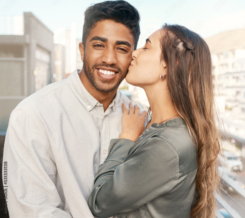 Happy couple, love and kiss on cheek from girlfriend bonding with boyfriend standing on a city building balcony on a holiday. Portrait of indian man and beautiful woman in interracial relationship Happy couple, love and kiss on cheek from girlfriend bonding with boyfriend standing on a city building balcony on a holiday. Portrait of indian man and beautiful woman in interracial relationship