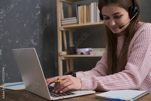 A girl with a headset works on a laptop. The topic of online work, support, training or remote communication