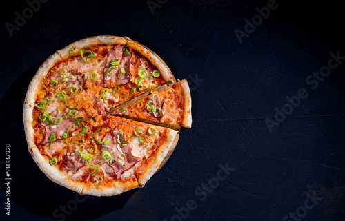 Delicious pizza with mozzarella cheese, ham, leeks on a tomato base on black background. Copy Space