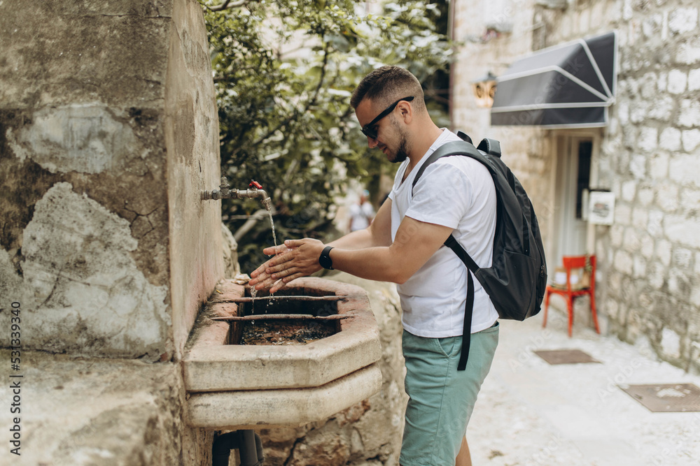 Man tourist, traveler wash his hands outside the street in old medieval tap and sink. Old town was listed UNESCO World Heritage Sites. King's Landing, capital of Seven Kingdoms in show Game of Thrones Man tourist, traveler wash his hands outside the street in old medieval tap and sink. Old town was listed UNESCO World Heritage Sites. King's Landing, capital of Seven Kingdoms in show Game of Thrones