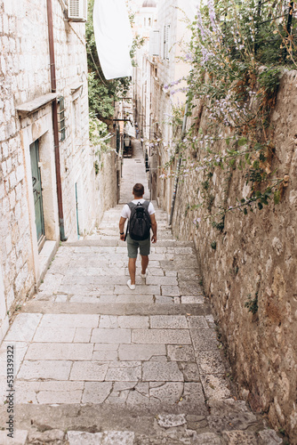 Man tourists and traveler walks in narrow dark street with greenery in old medieval town, listed UNESCO World Heritage Sites. King's Landing, capital of Seven Kingdoms in show Game of Thrones