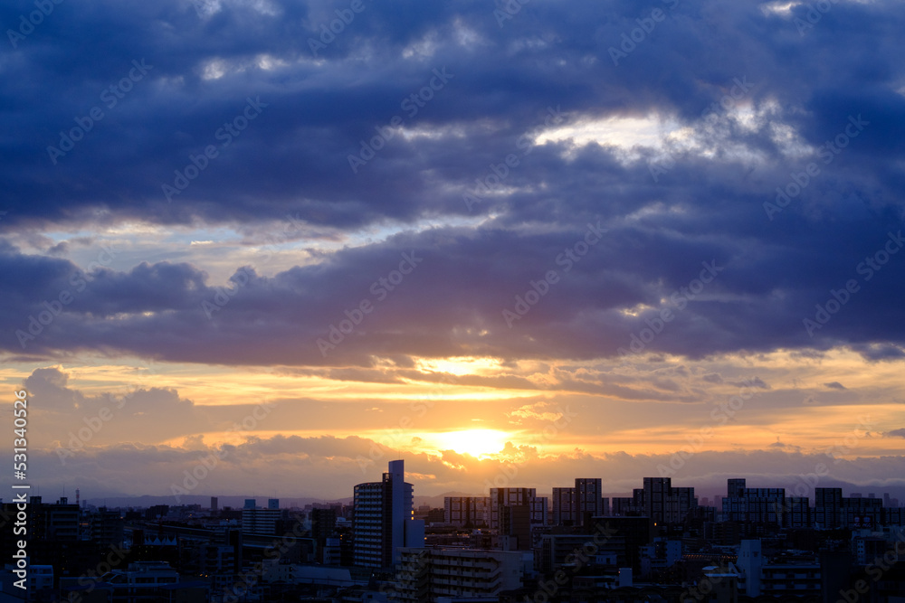 厚い雲に覆われた東の空から太陽が姿を表し。高層ビルがシルエットで浮かび上がる。早朝神戸市内より芦屋大阪方面を臨む。