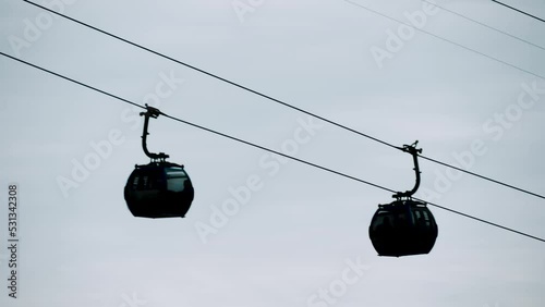 Ropeway, cable car cabins silhouettes are moving against gray sky in Batumi, Georgia - aerial rope transit, gondola lift - overcast. Tourism, cableway, sightseeing and public transportation concept photo