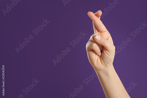 Woman holding fingers crossed on purple background, closeup with space for text. Good luck superstition