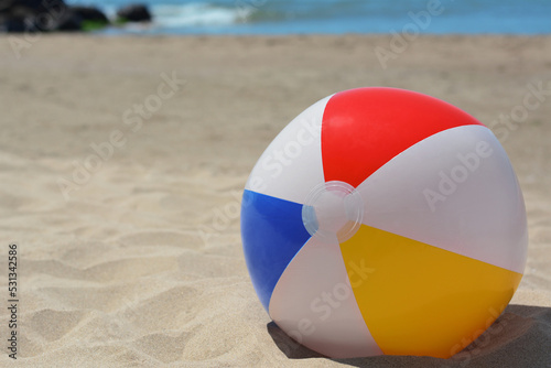Colorful beach ball on sand near sea, space for text