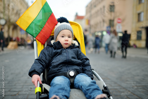 Adorable toddler boy celebrating Lithuanian Independence Day holding tricolor Lithuanian flag in Vilnius