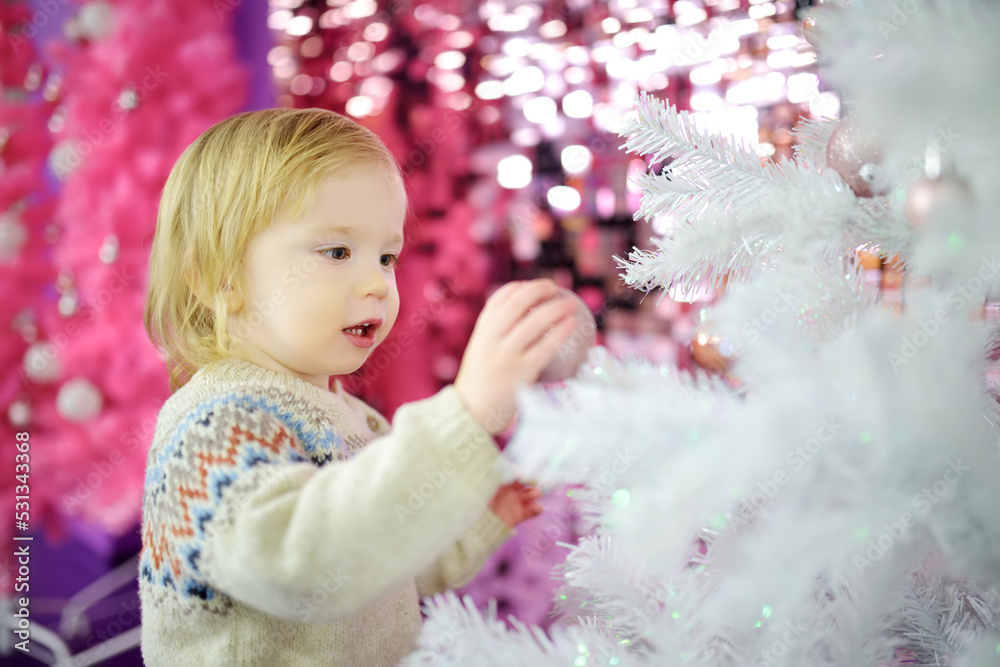Fototapeta premium Happy little toddler boy playing with Chistmas lights in a cozy living room on Christmas eve. Celebrating Xmas at home.