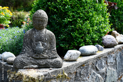 An image of a small stone Buddha statue in a tranquil flower garden. 