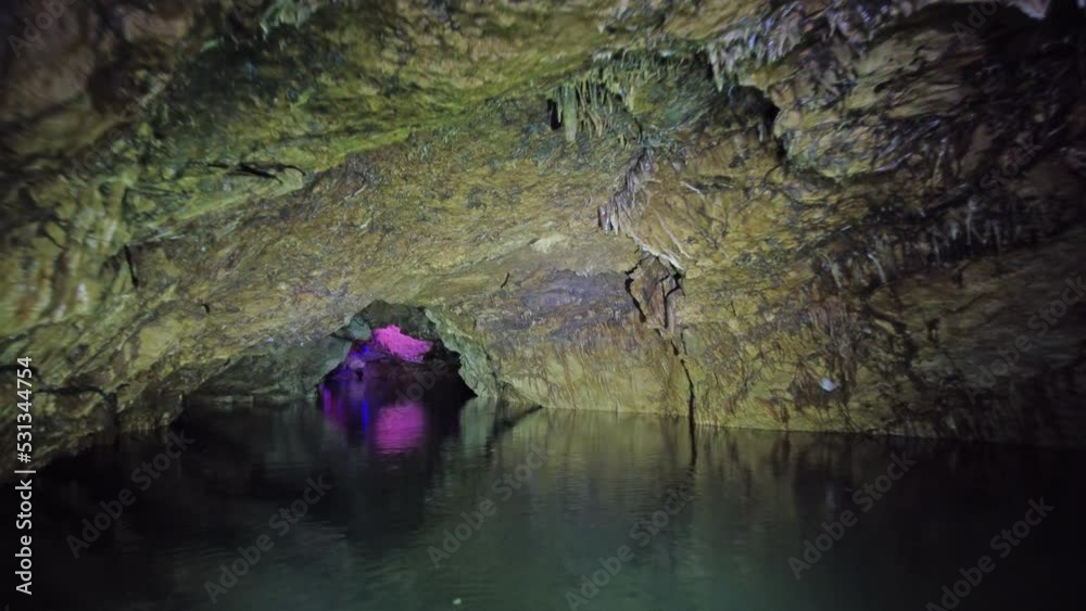 Boating on the underground river in a dark stone cave in magic multicolor light, 4k