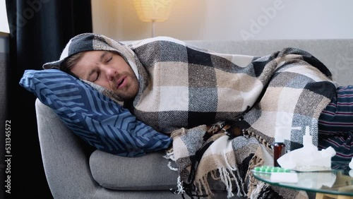 Period of seasonal diseases. Close up of a sick man with flu, fever and headache lying wrapped in a plaid on the couch. Concept of viral diseases photo