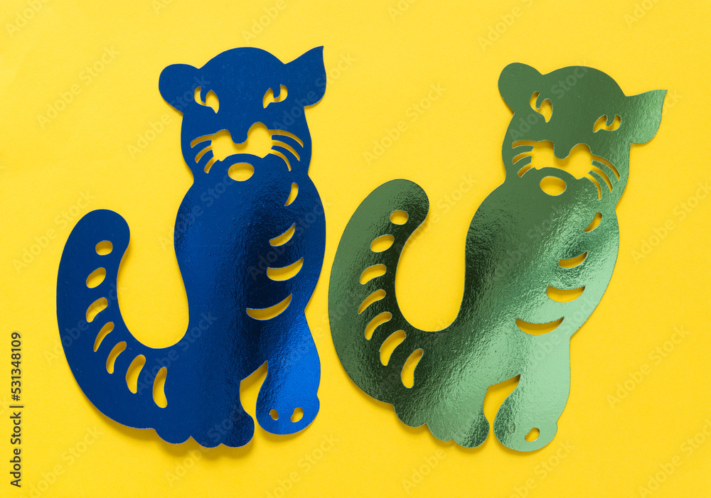 two metallic foil paper silhouettes of big cats (tiger or jaguar) isolated on yellow paper