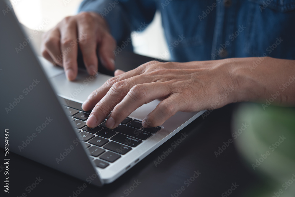 Closeup of a business man's hands working and typing on laptop computer keyboard on wooden table Closeup of a business man's hands working and typing on laptop computer keyboard on wooden table