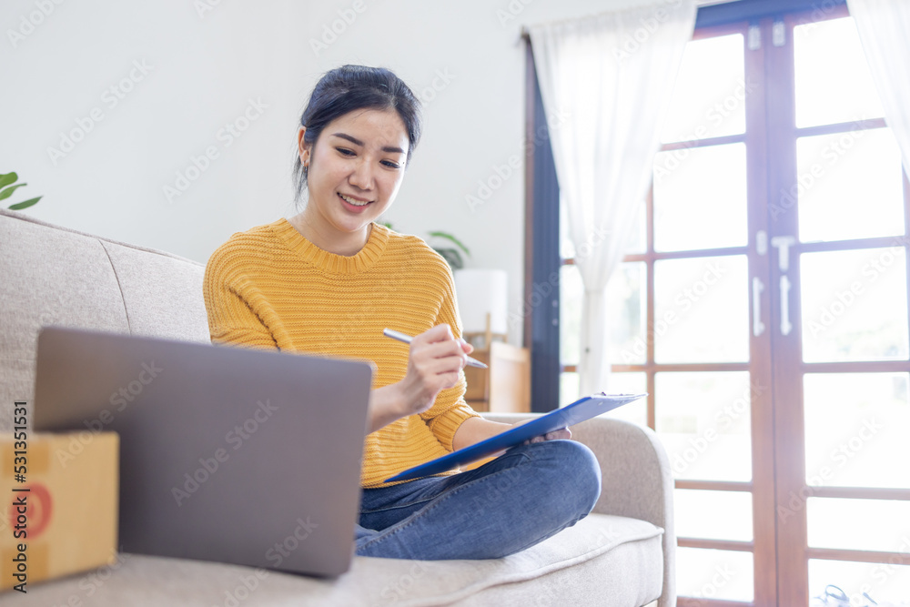Business Asian women sit on sofa use laptop computer checking customer order online shipping box at home. Starting Small business entrepreneur SME freelance. Online business, Work at home SME concept. Business Asian women sit on sofa use laptop computer checking customer order online shipping box at home. Starting Small business entrepreneur SME freelance. Online business, Work at home SME concept.