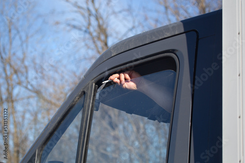 Male hand with cigarette throws ash from slightly open window of vehicle.