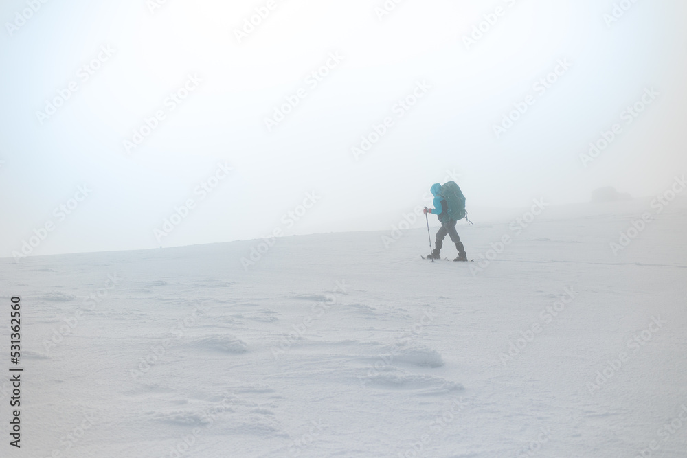 girl with a backpack and snowshoes walks through the snow during a snow storm.