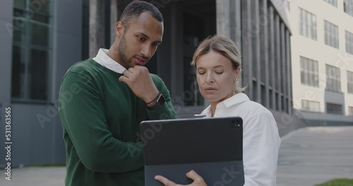 Attractive Businessman and Businesswoman Discussing Project Outside Together at Urban Street. Serious Business Couple Outdoors Examining Tablet Screen