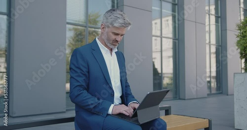 Mature Businessman in Official Suit Sitting on Bench Before Meeting With Partners. Mature Guy Preparing to Make Presentation. Office Clerk Working on Tablet Outdoors 