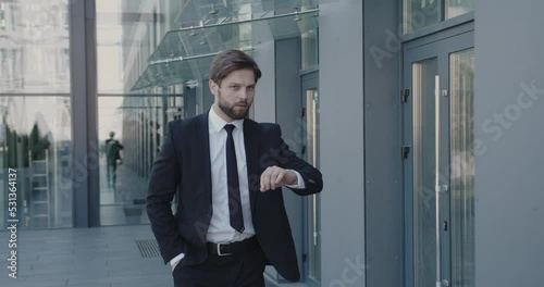 Caucasian Businessman Going at the Street with Office Center at the Background. Professional Looking at Wristwatch and Hurry Up. Outside 