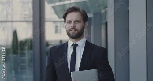 Smart Man Holding Laptop and Looking at the Camera, Smiling. Medium Portrait of Handsome Entrepreneur Standing on Street. People Emotions Concept