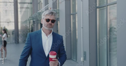 Business Person Holding Coffee To Go Having Break. Senior Businessman Walking On Street. Mature Guy Enjoying Hot Beverage Near Office Building. Business and Lifestyle Concept 