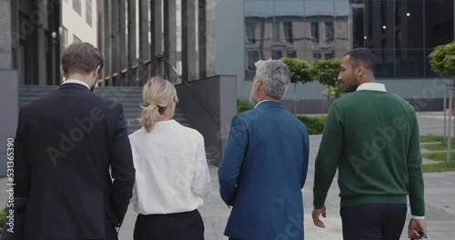 Back View of Business People Going From Work and Discussing Project. Four Partners in Formal Wear Walking Along the Street During the Break at Office, Urban Background