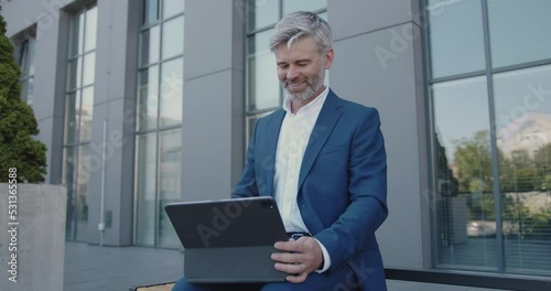 Handsome Businessman Talking Via Video Chat on his Tablet. Grey Haired Man Executive Smiling Confident While Having Video Call at Street. Video Call Concept 