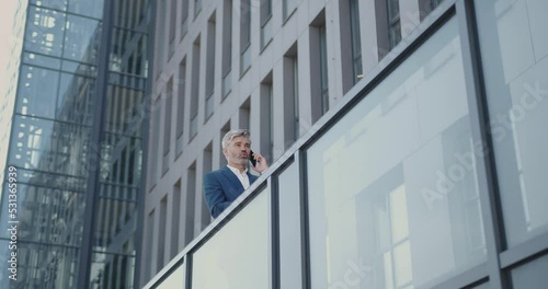 Senior Professional Talking on Phone. Bottom View of Caucasian Businessman Standing at the Street with Office Center at the Background. Outside 