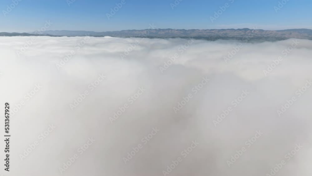 Drone shot of thick, milky clouds above the valley. Majestic blue skyline with mountain range in the background as seen from top. High quality 4k footage
