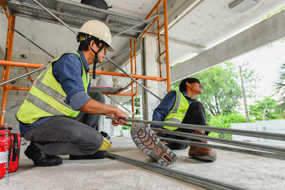 Accident in the construction workplace, Electrical metal conduit pipe falls on an unsuspecting builder's leg, Foreman to helping injured colleague or builder with first aid bag in construction site Accident in the construction workplace, Electrical metal conduit pipe falls on an unsuspecting builder's leg, Foreman to helping injured colleague or builder with first aid bag in construction site