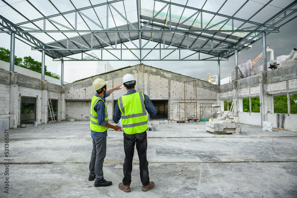 Civil engineers discuss with foreman or builder while holding blueprints and standing under steel structure roof of building at construction site, Consultant in construction site jobs concept.
