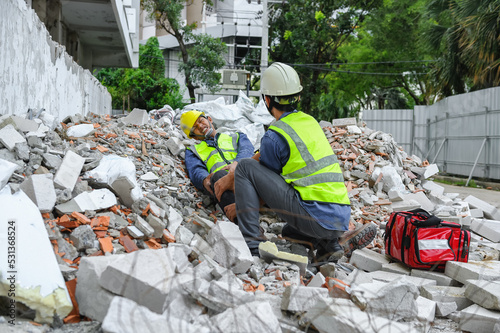 Accident in construction workplace, Knee accident from slip or stumble fall on the concrete scrap at construction site. Foreman to helping injured colleague with first aid bag, Unsafe in workplace.