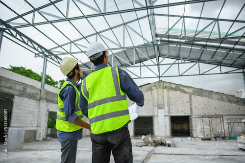 Civil engineers discuss with foreman or builder while holding blueprints and standing under steel structure roof of building at construction site, Consultant in construction site jobs concept.