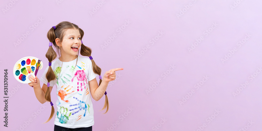 A little artist points to your advertisement on a pink isolated background. The child holds a palette of colorful paints and brushes for drawing. Art courses for schoolchildren. A little artist points to your advertisement on a pink isolated background. The child holds a palette of colorful paints and brushes for drawing. Art courses for schoolchildren.
